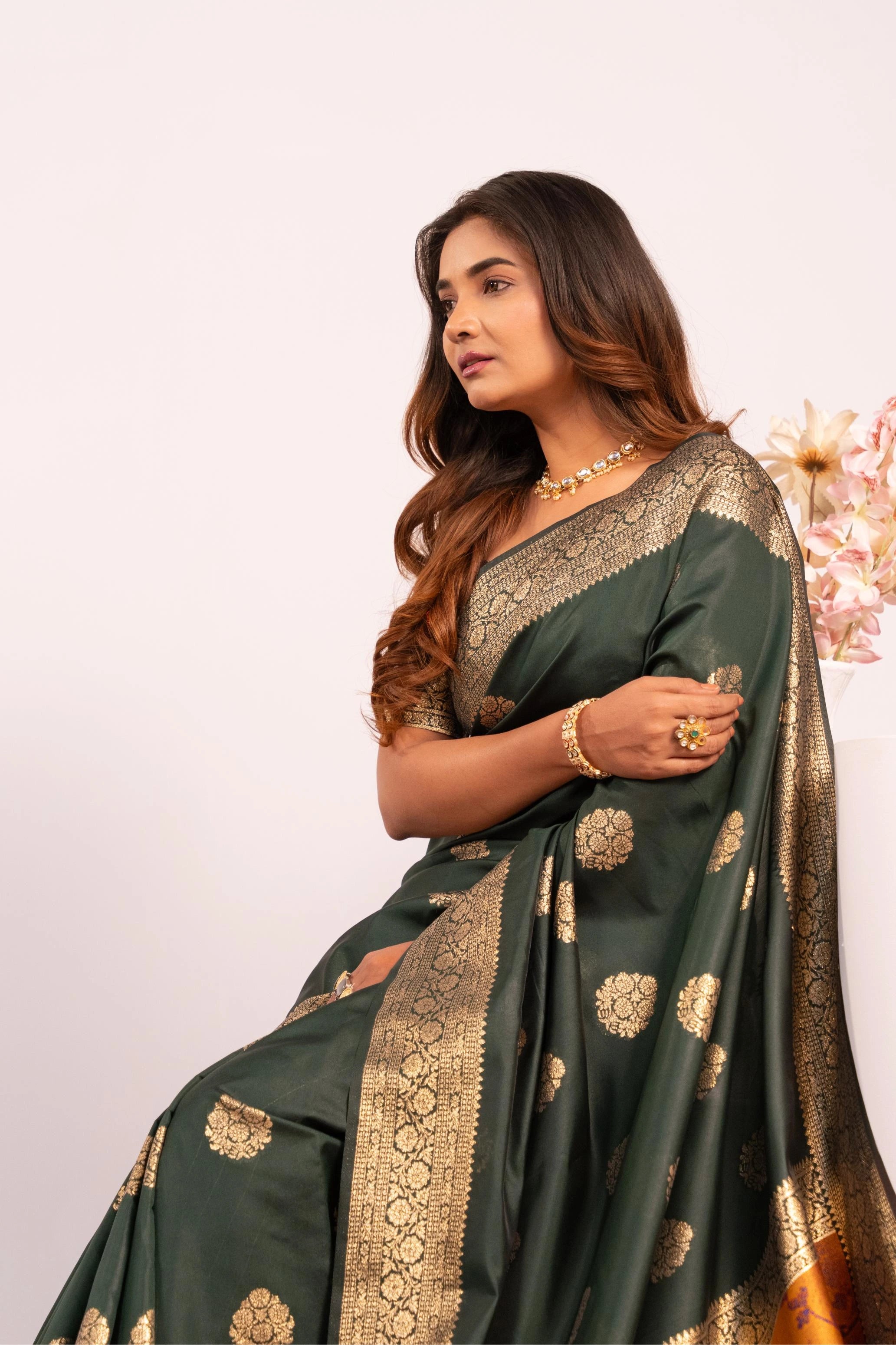 Woman wearing a dark green saree with gold patterns on a light background