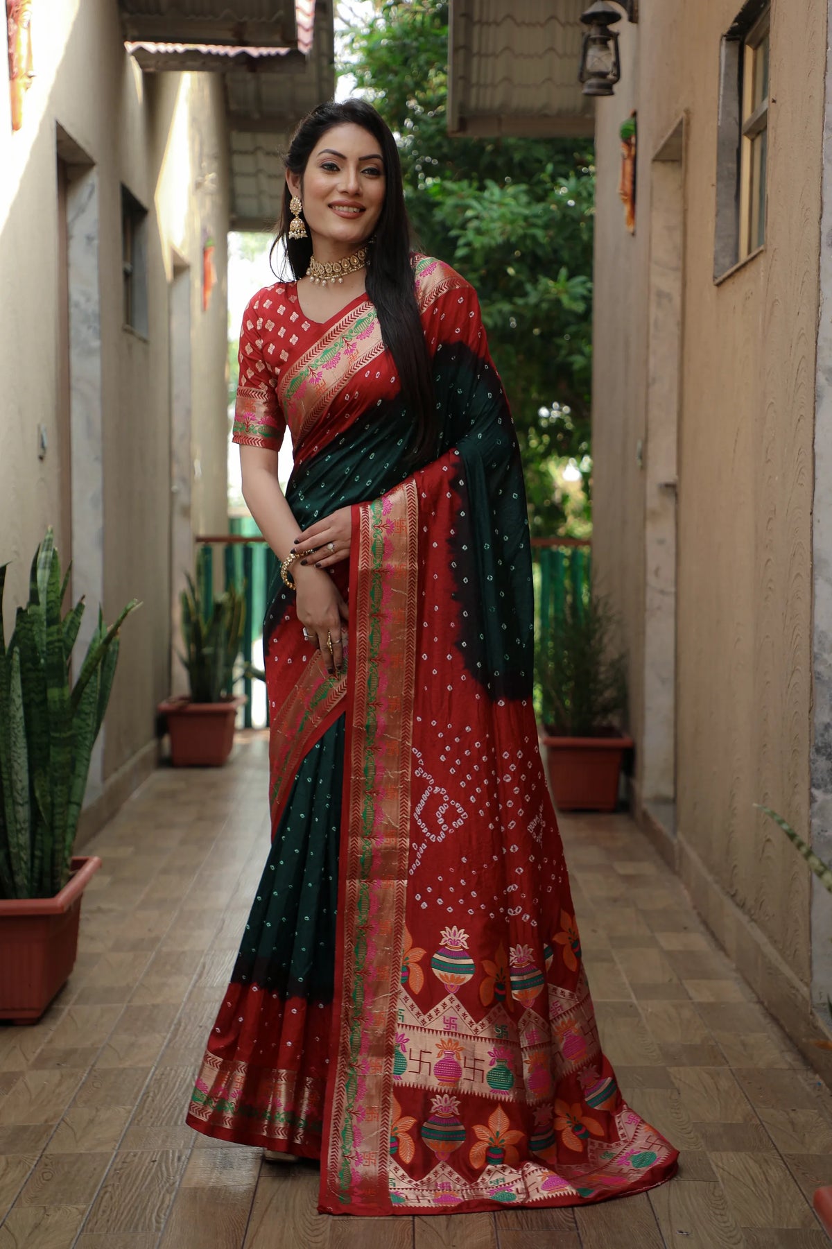 Woman in a red and green saree standing in a narrow alleyway.