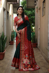 Woman in a red and green saree standing in a narrow alleyway.
