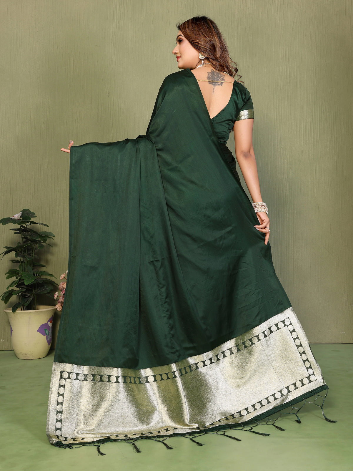Woman wearing a dark green saree with a white border on a plain background