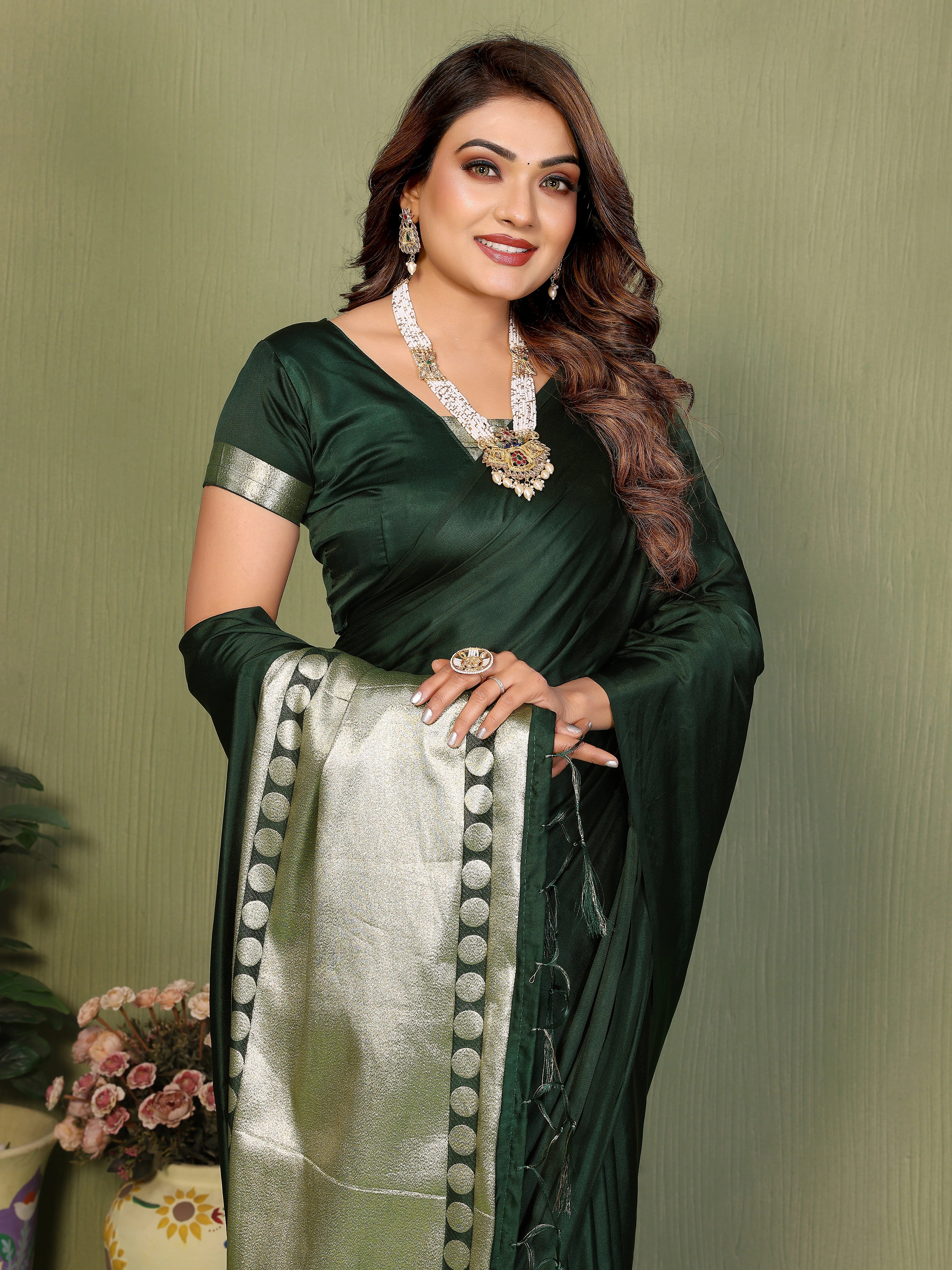 Woman wearing a green saree with a white border against a plain background