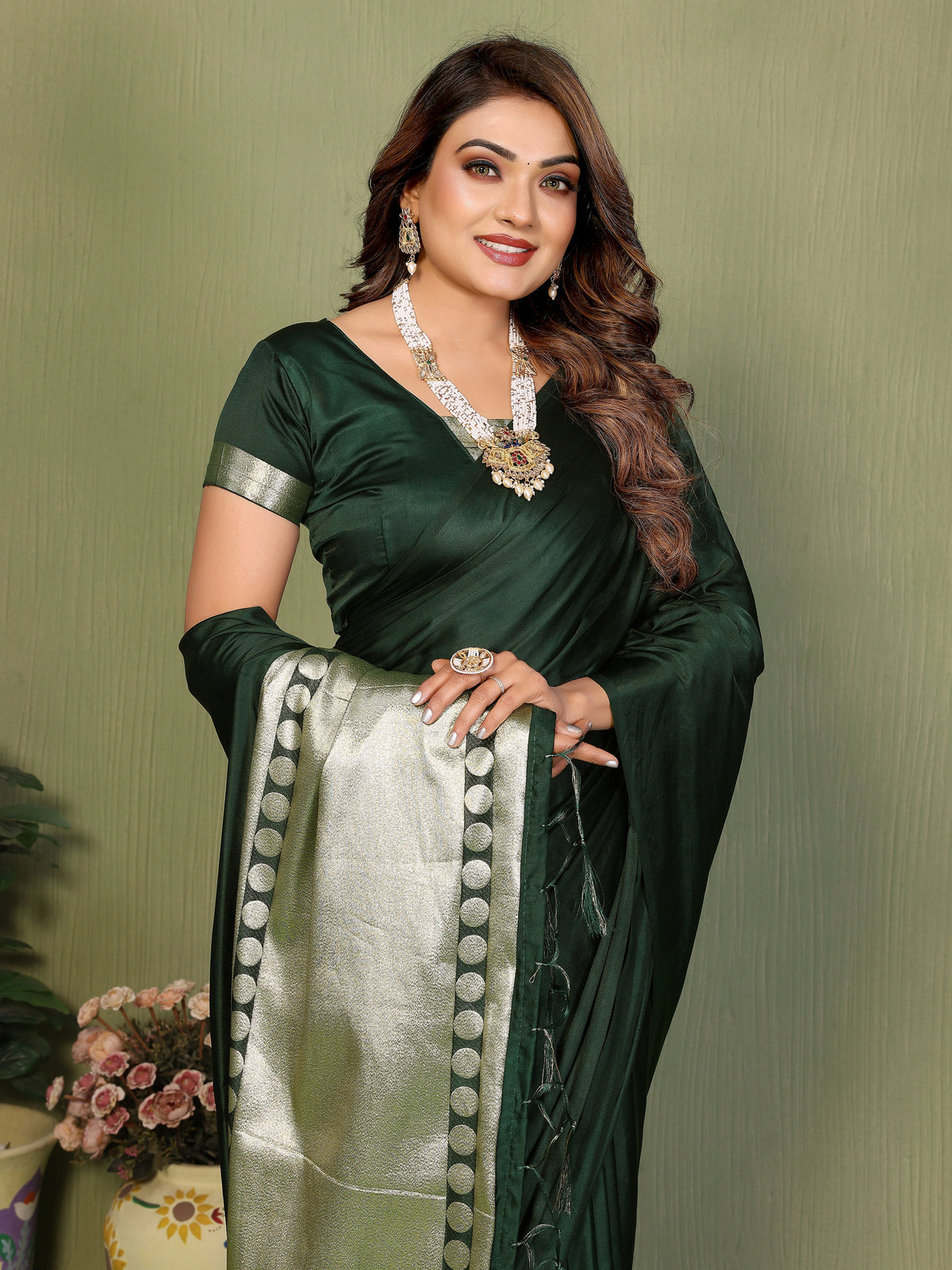 Woman wearing a green saree with a white border against a plain background