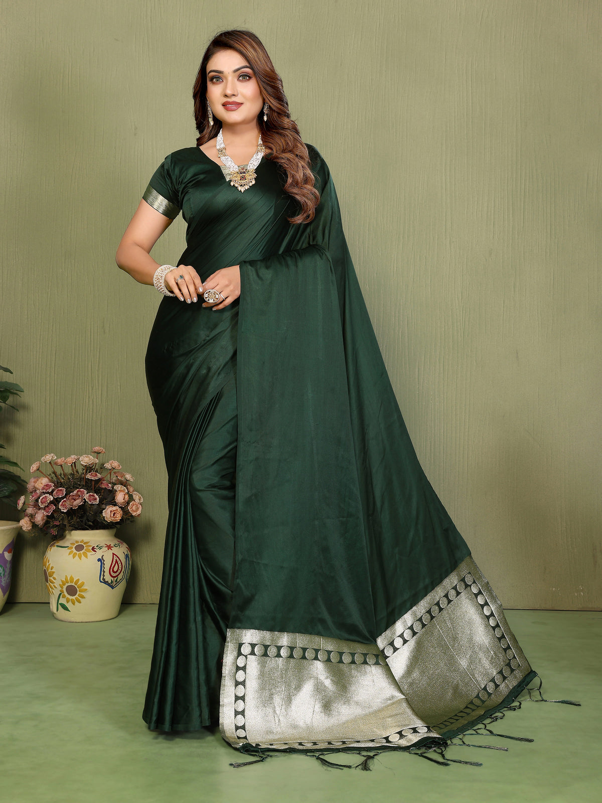 Woman wearing a dark green saree with silver border against a plain background