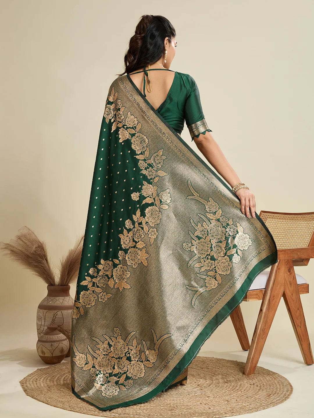 Woman wearing a green saree with gold embroidery, standing against a beige background.