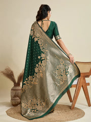 Woman wearing a green saree with gold embroidery, standing against a beige background.