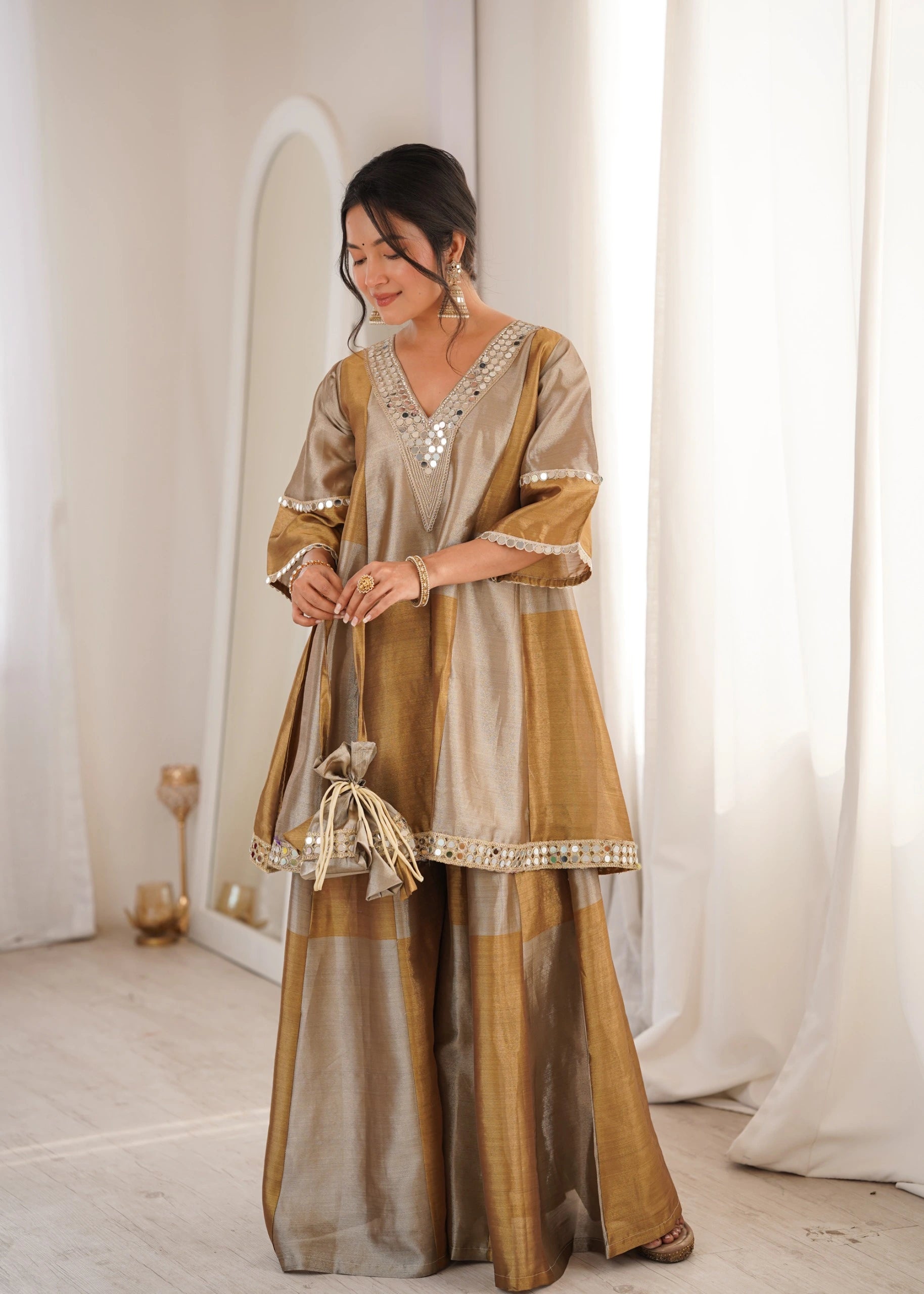 Woman wearing a traditional outfit with a gold and beige color scheme in a minimalistic setting.