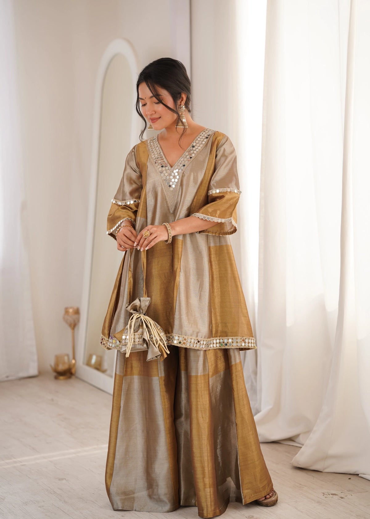 Woman wearing a traditional outfit with a gold and beige color scheme in a minimalistic setting.