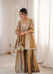Woman wearing a traditional outfit with a gold and beige color scheme in a minimalistic setting.