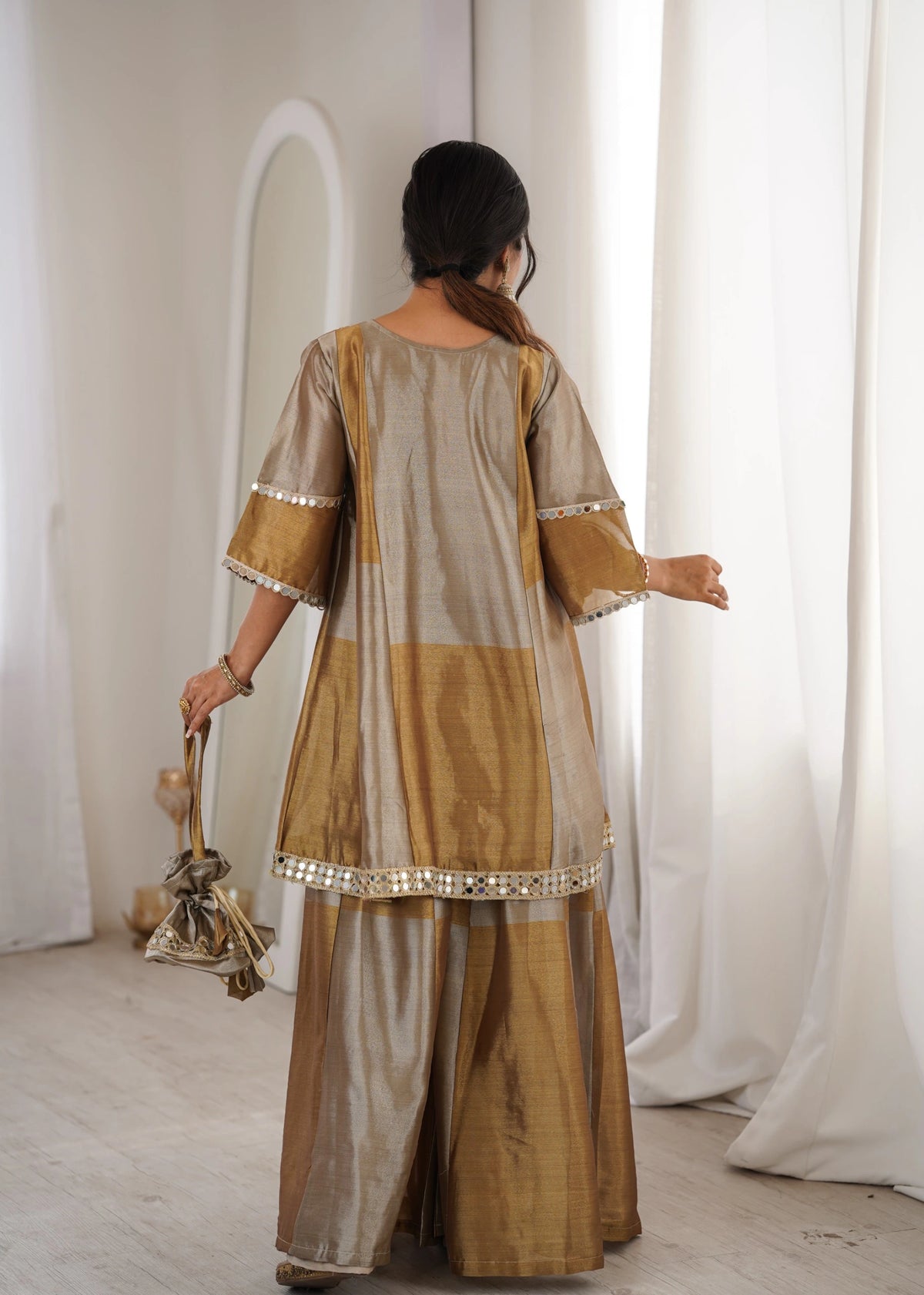 Woman wearing a traditional outfit with gold and beige colors in a minimalistic setting.