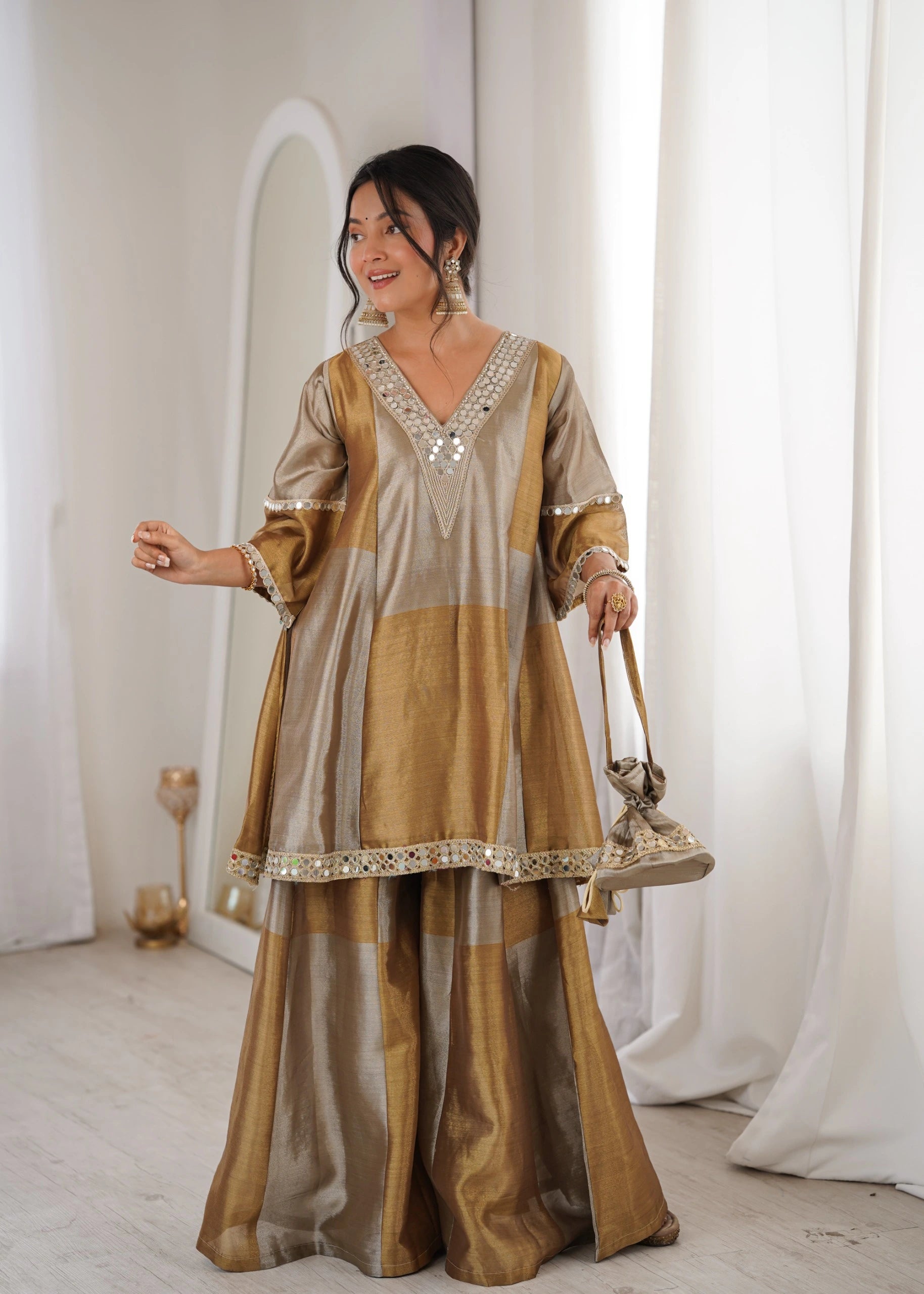 Woman in a traditional outfit standing in a softly lit room with white curtains.