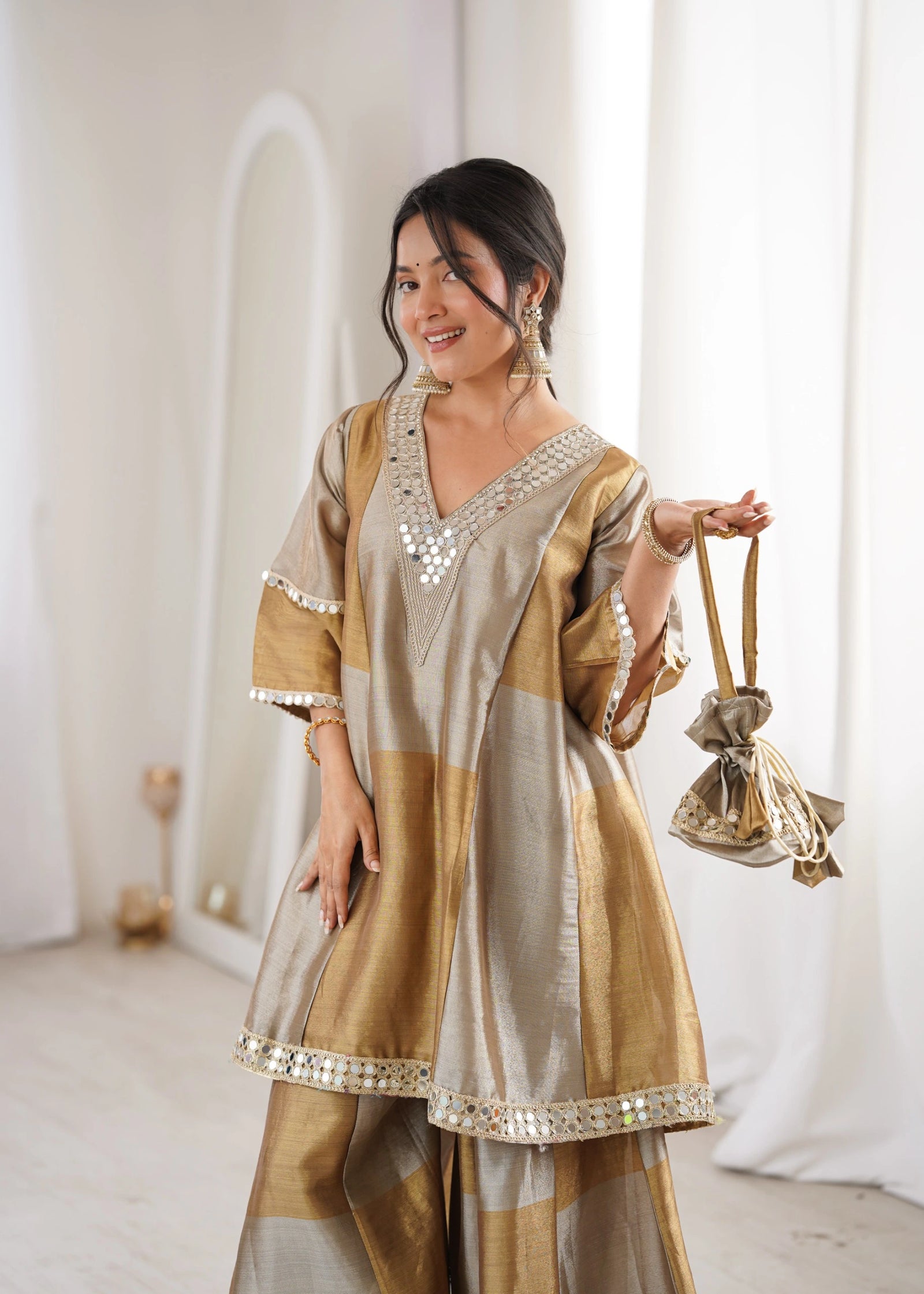 Woman in a traditional outfit holding a handbag in a bright room
