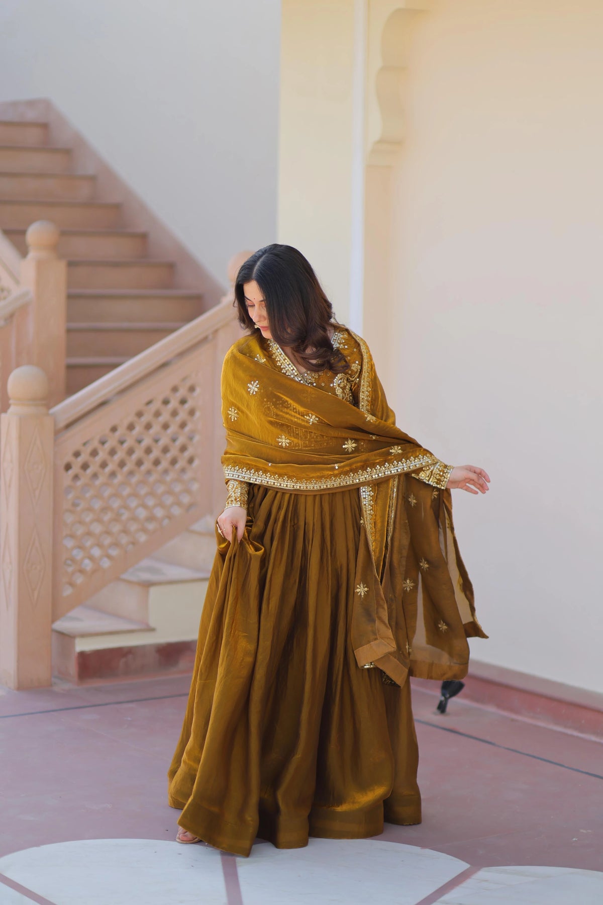 Woman in a long, flowing dress standing in a room with wooden stairs and white walls.