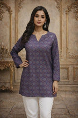 Woman wearing a patterned purple kurta with white pants in an ornate room.