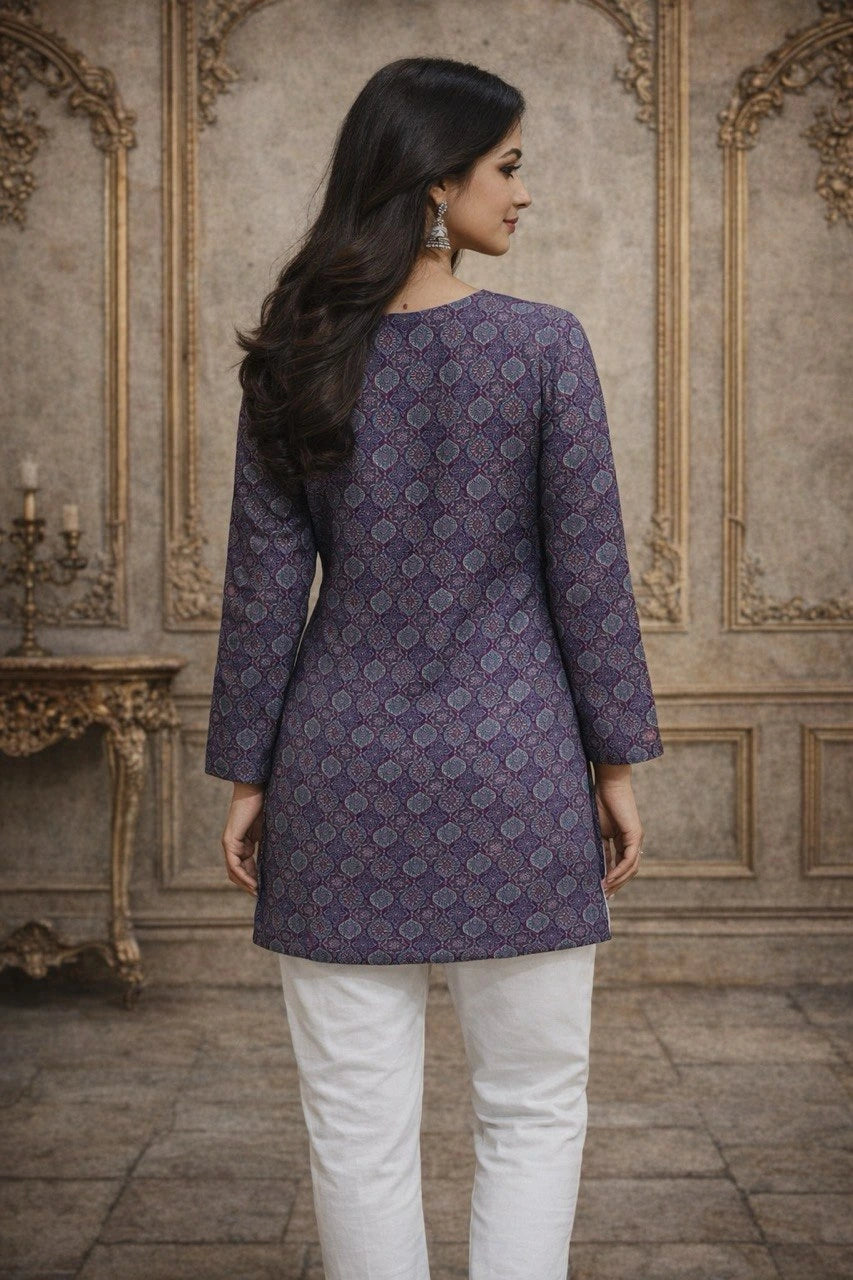 Woman wearing a patterned purple top and white pants in an ornate room.