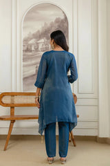 Woman in a blue outfit standing in a room with a wooden bench and framed picture on the wall.
