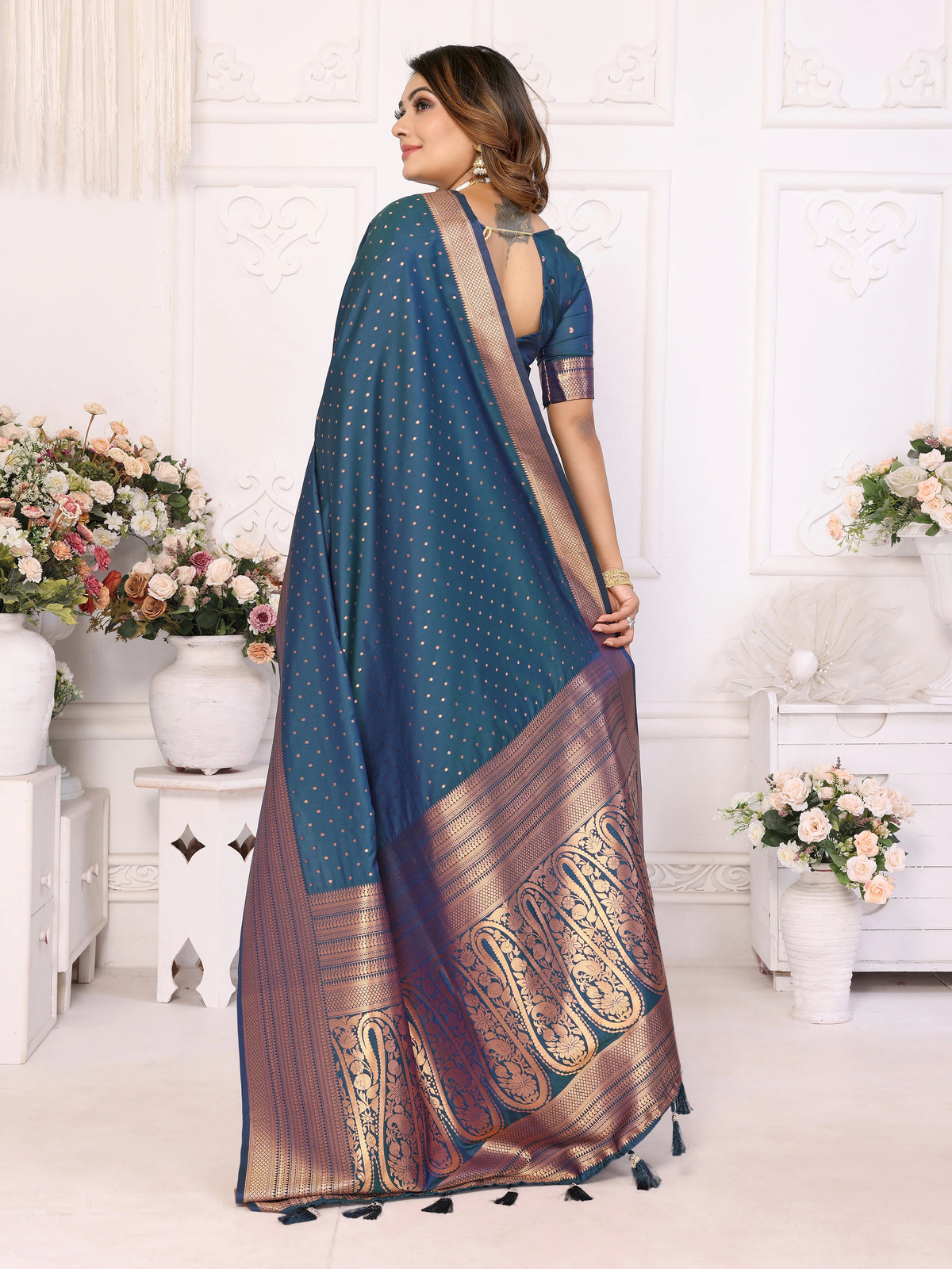 Woman wearing a blue saree with gold patterns in a decorated room.