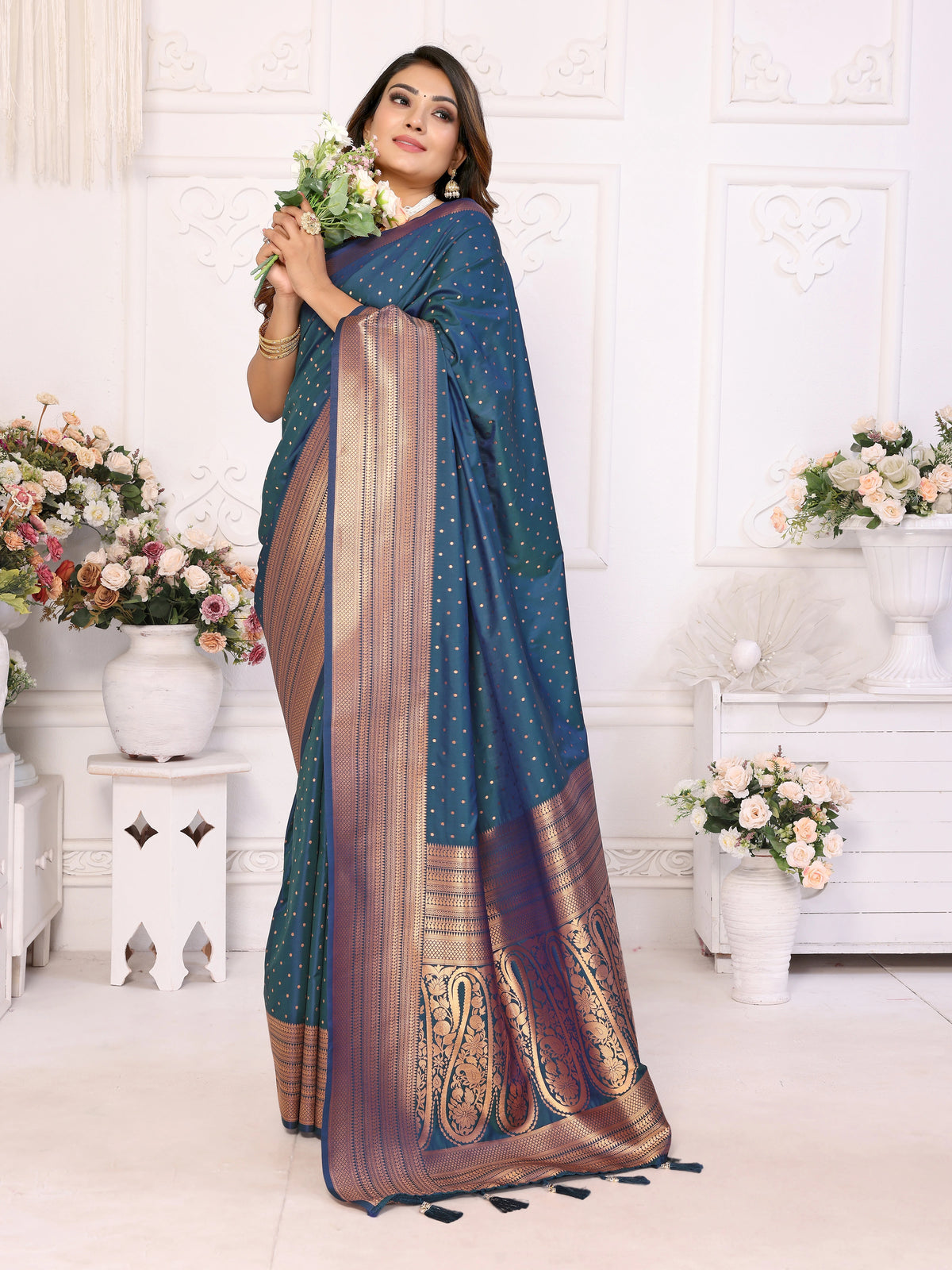 Woman wearing a blue and brown saree with floral decorations in a decorated room.