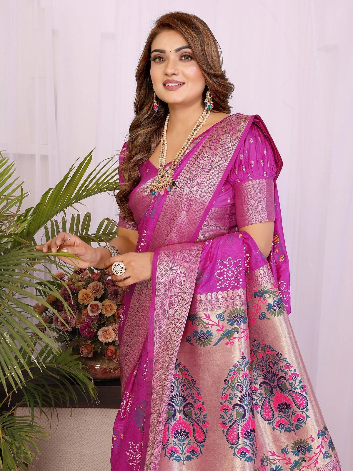 Woman wearing a pink saree with floral patterns, holding a plant and flowers.