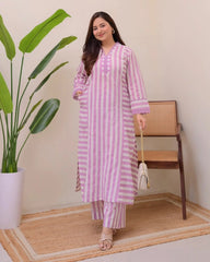 Woman wearing a pink and white striped outfit standing next to a plant and chair.