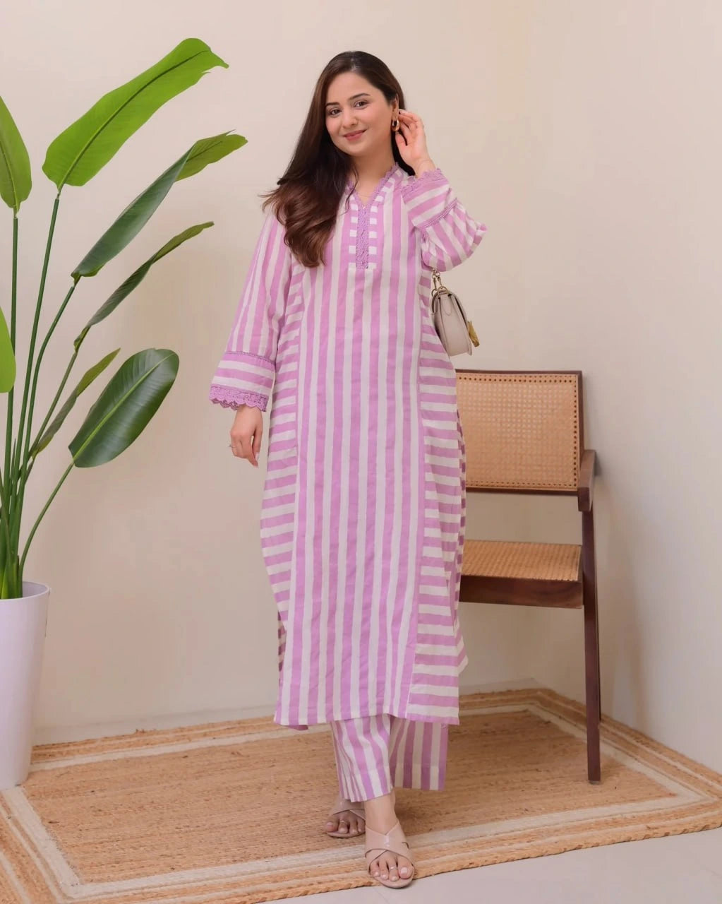 Woman in a pink and white striped outfit standing in a room with a plant and chair.