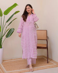 Woman in a pink and white striped outfit standing in a room with a plant and chair.