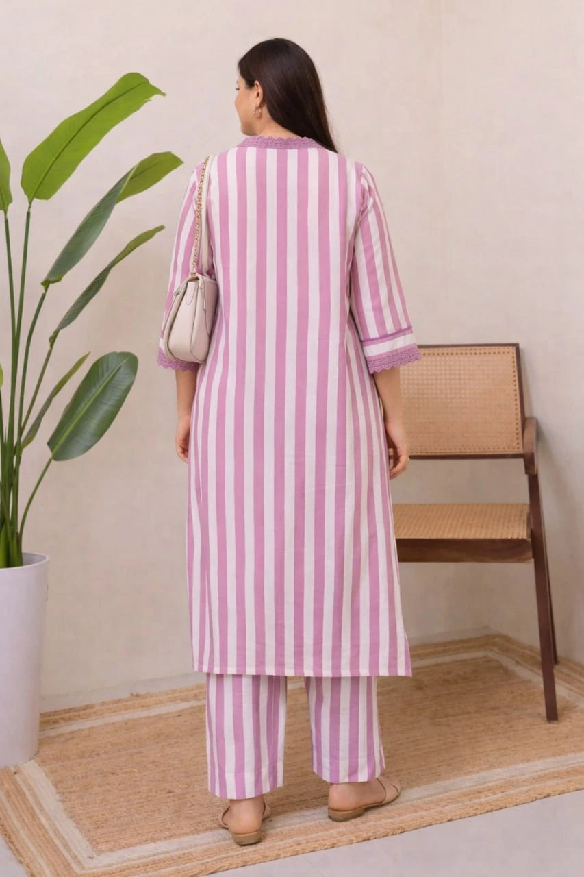 Woman wearing a pink and white striped outfit standing in a room with a plant and chair.