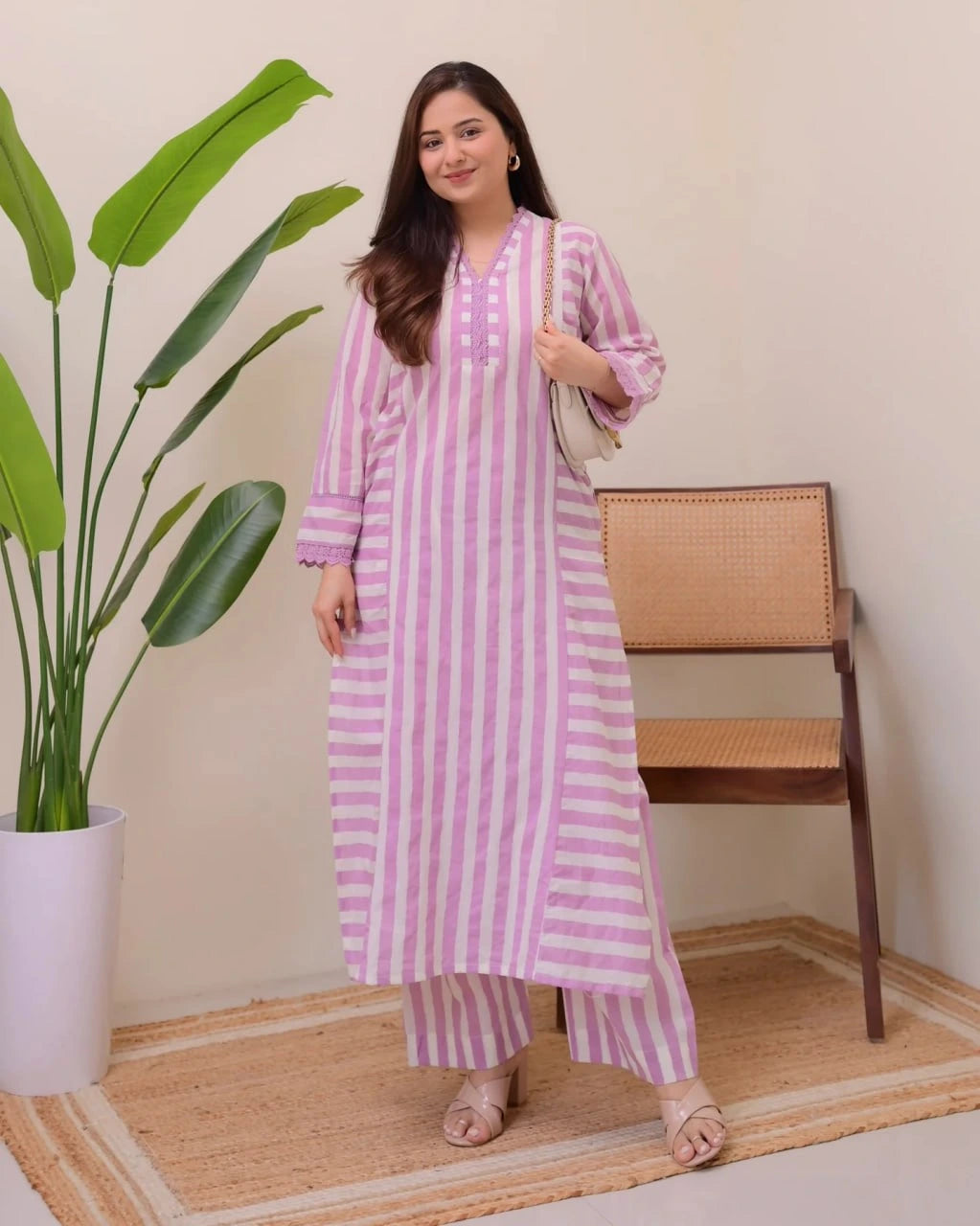 Woman in a pink and white striped outfit standing next to a plant and chair.