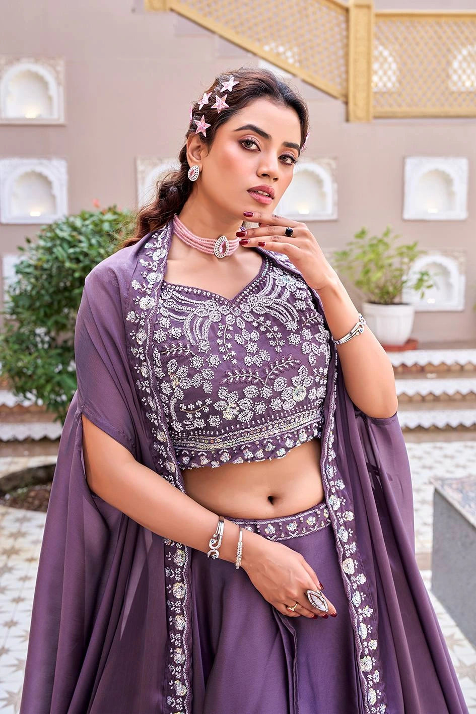 Woman in a traditional outfit with intricate designs, standing in an outdoor setting.