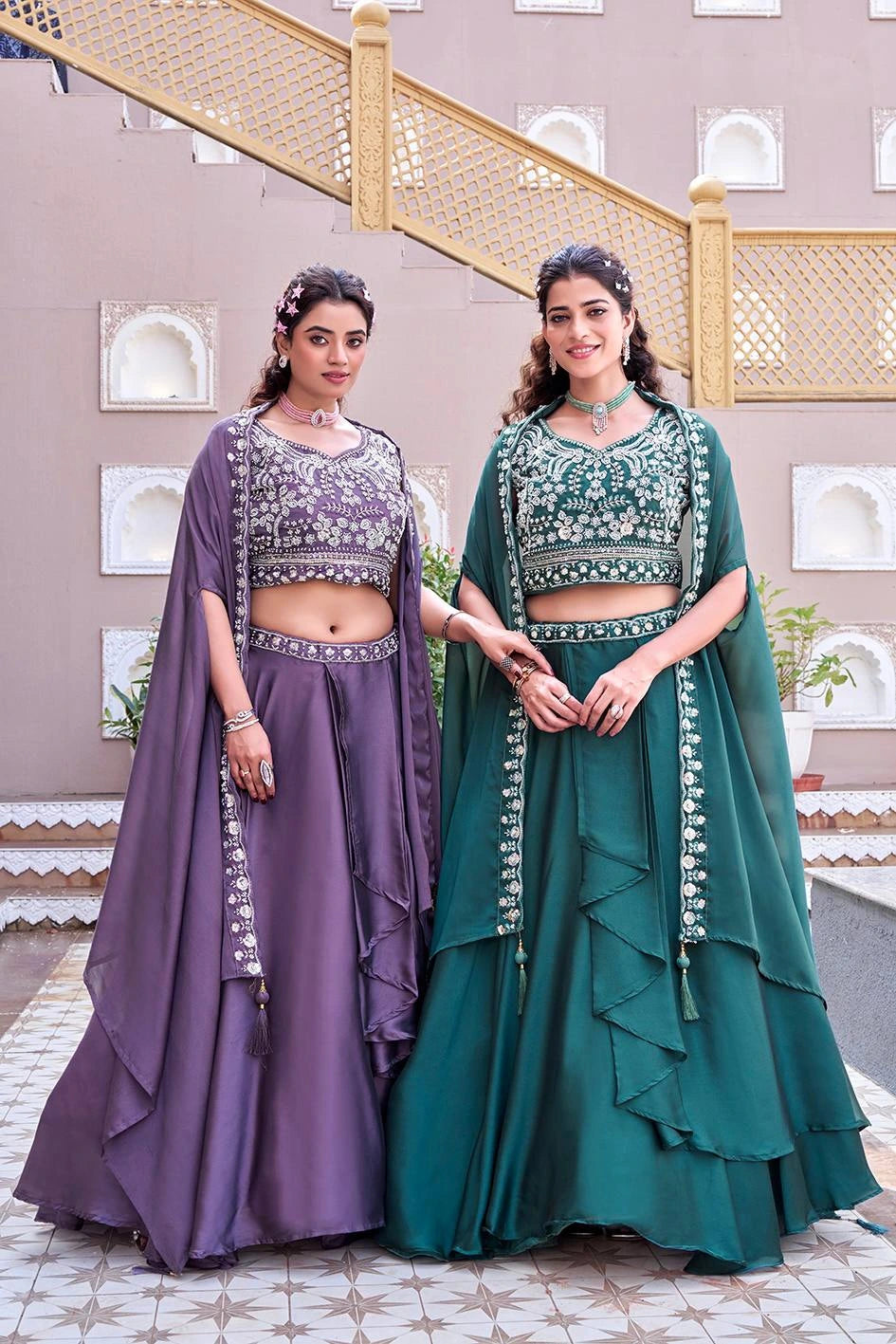 Two women in traditional outfits standing indoors with decorative elements in the background.