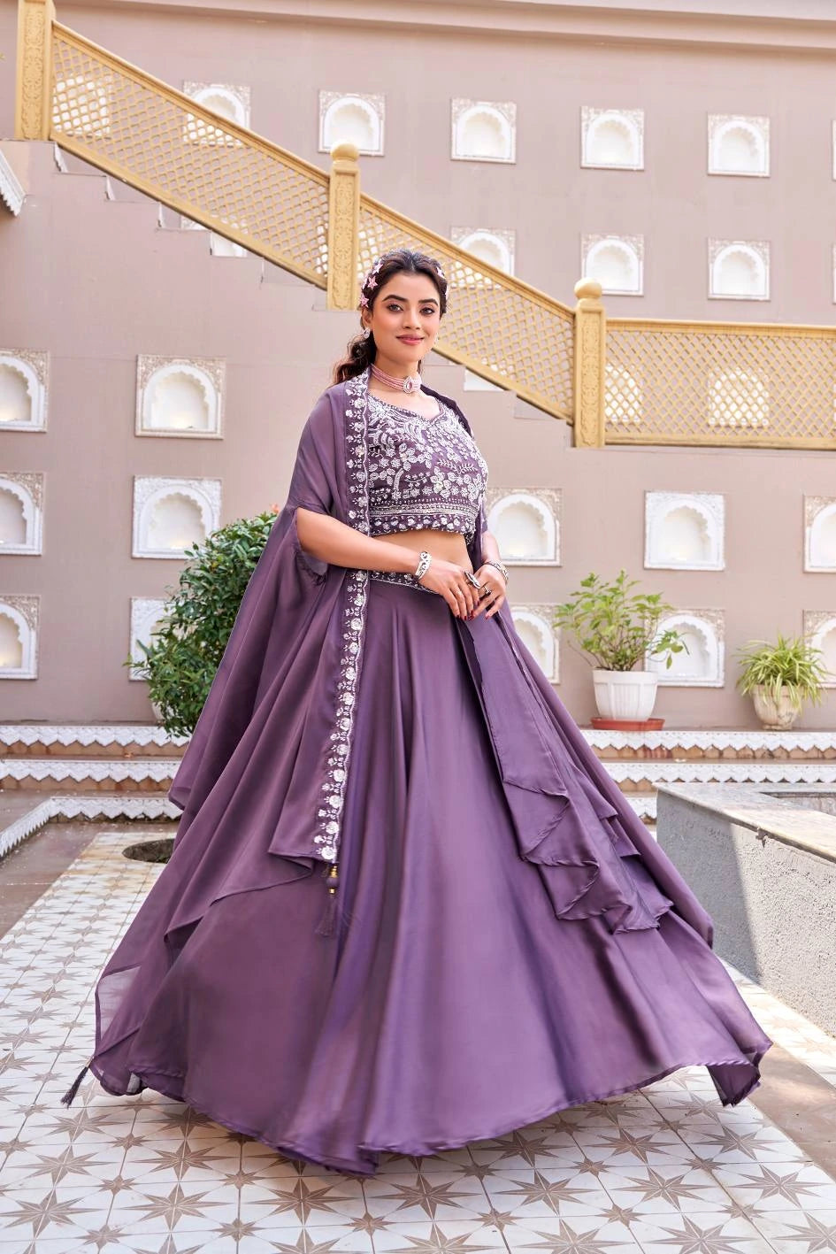 Woman in a purple traditional outfit standing in front of a decorative wall with plants.