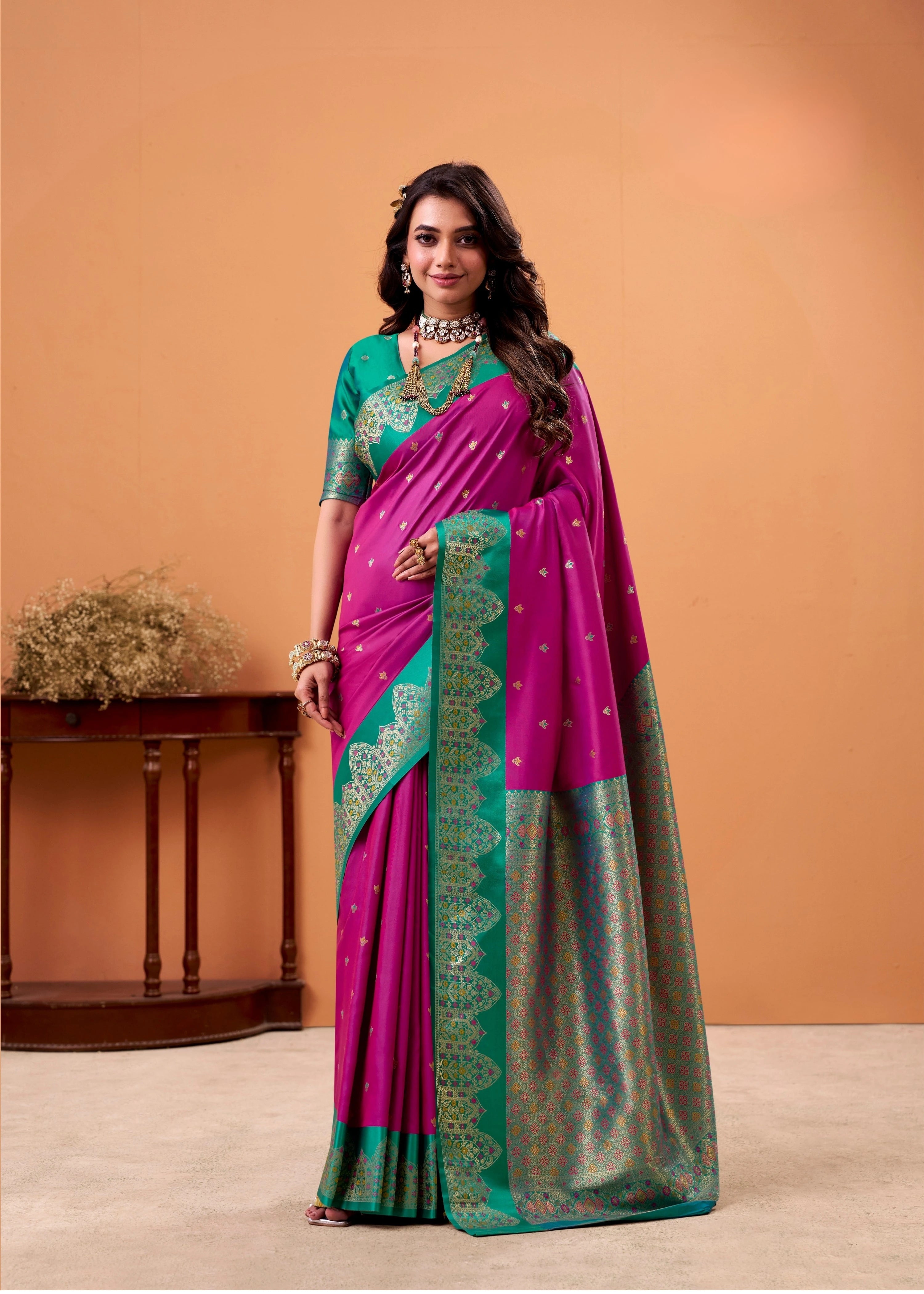 Woman wearing a pink and green saree with a matching blouse against an orange background