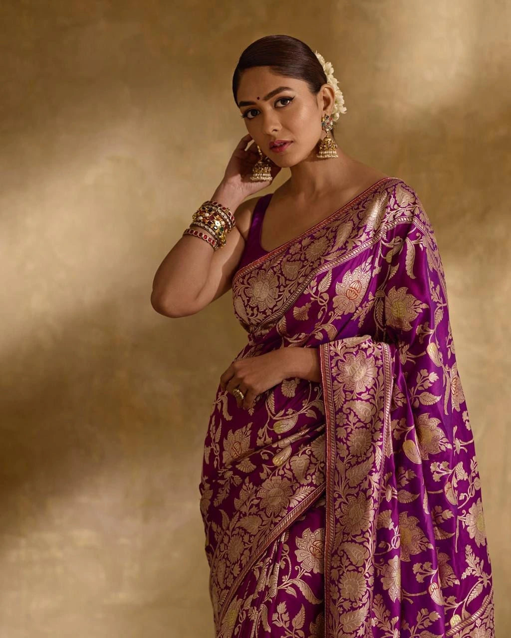 Woman wearing a purple and gold saree with jewelry against a beige background
