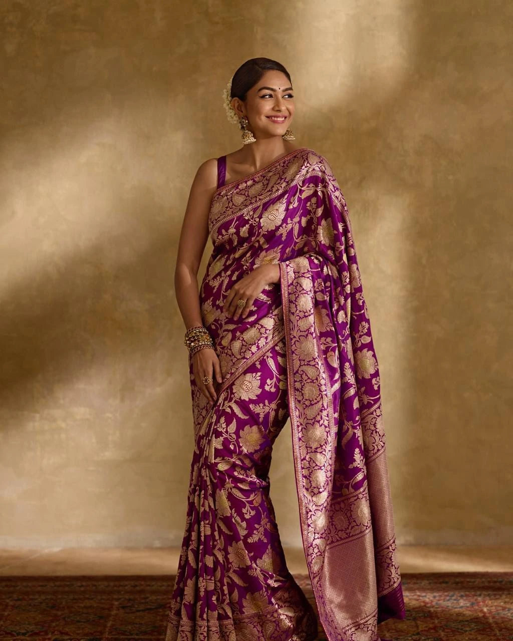 Woman wearing a purple and gold saree against a beige background