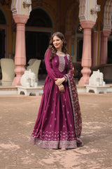 Woman in a purple traditional outfit standing in front of decorative architecture.