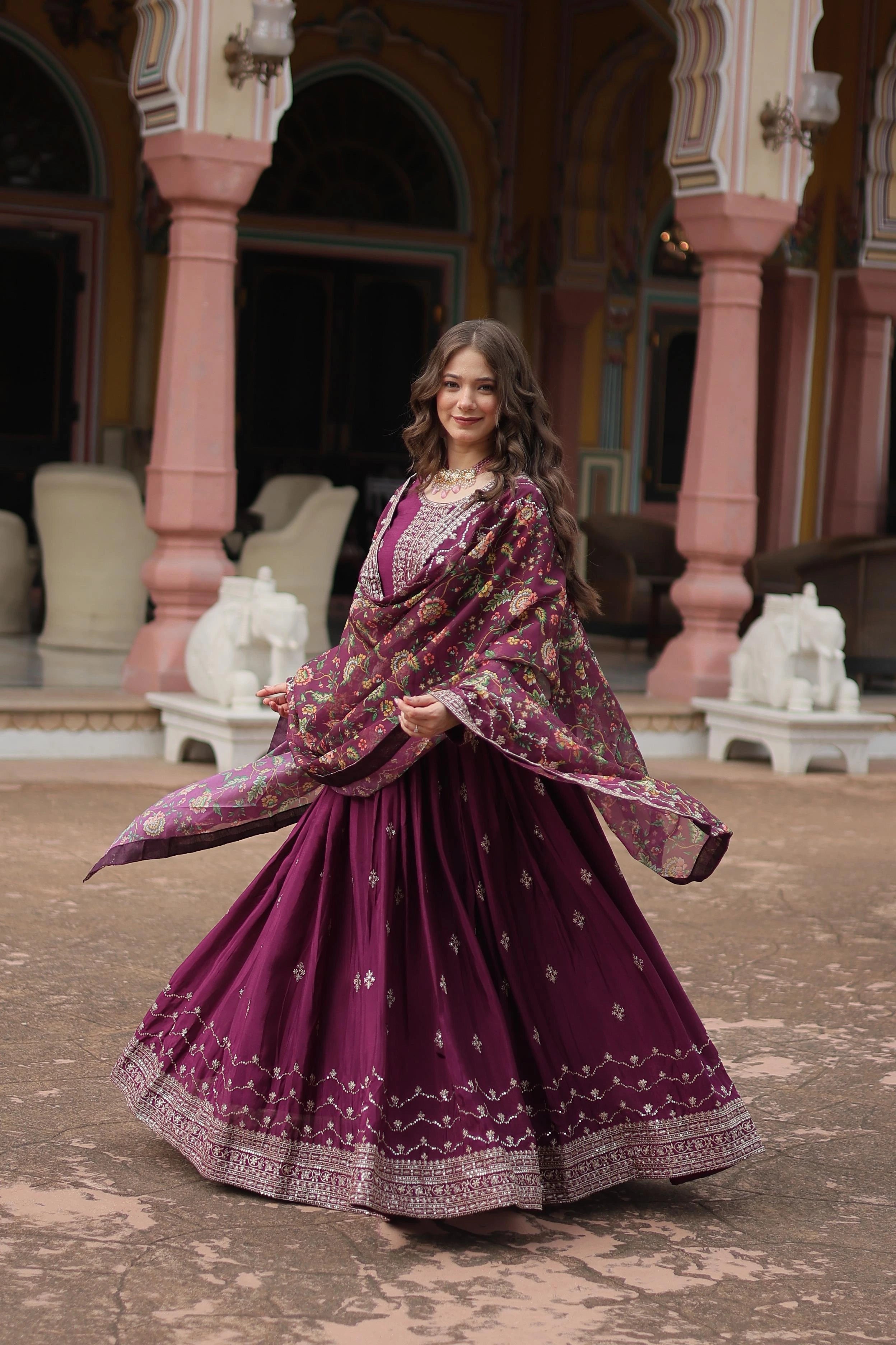 Woman in a traditional purple outfit with floral patterns standing in an ornate outdoor setting.