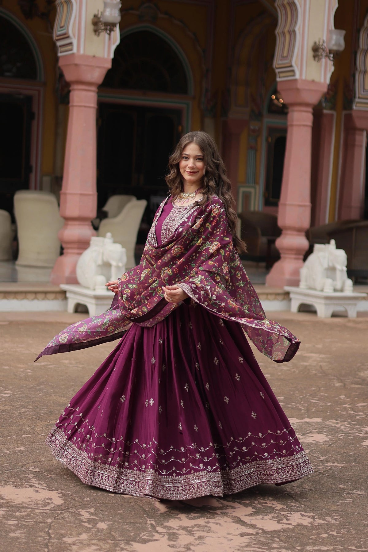 Woman in a traditional purple outfit with floral patterns standing in an ornate outdoor setting.