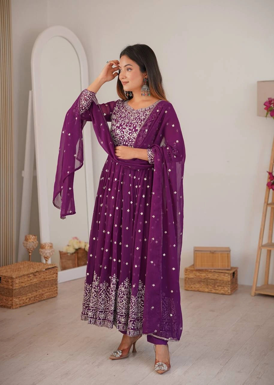 Woman in a purple traditional outfit with white patterns in a minimalistic room.
