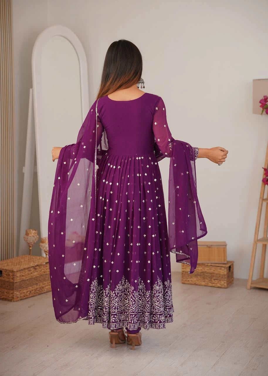 Woman wearing a purple dress with a sheer overlay in a room setting.