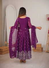 Woman wearing a purple dress with a sheer overlay in a room setting.
