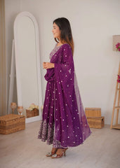 Woman in a purple traditional outfit standing in a room with a mirror and decorative items.
