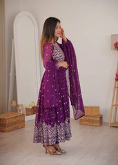 Woman in a purple traditional outfit with white patterns in a minimalistic room.
