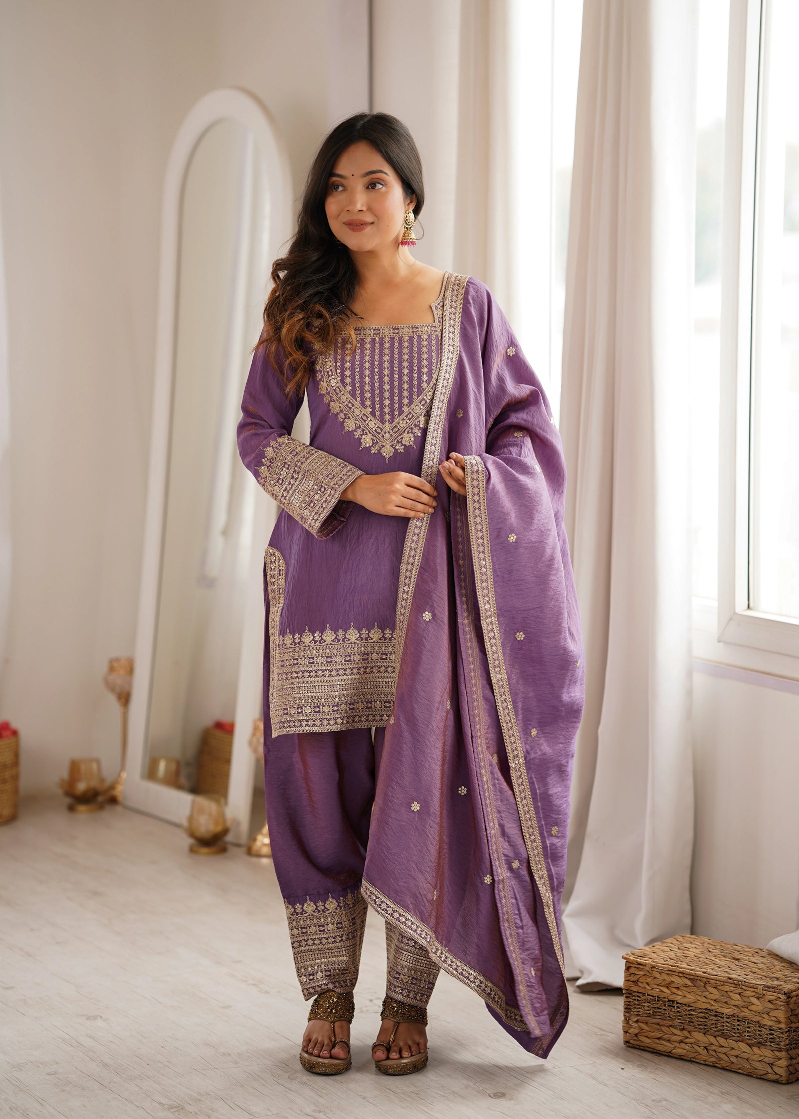 Woman wearing a purple traditional outfit with intricate designs in a bright room.