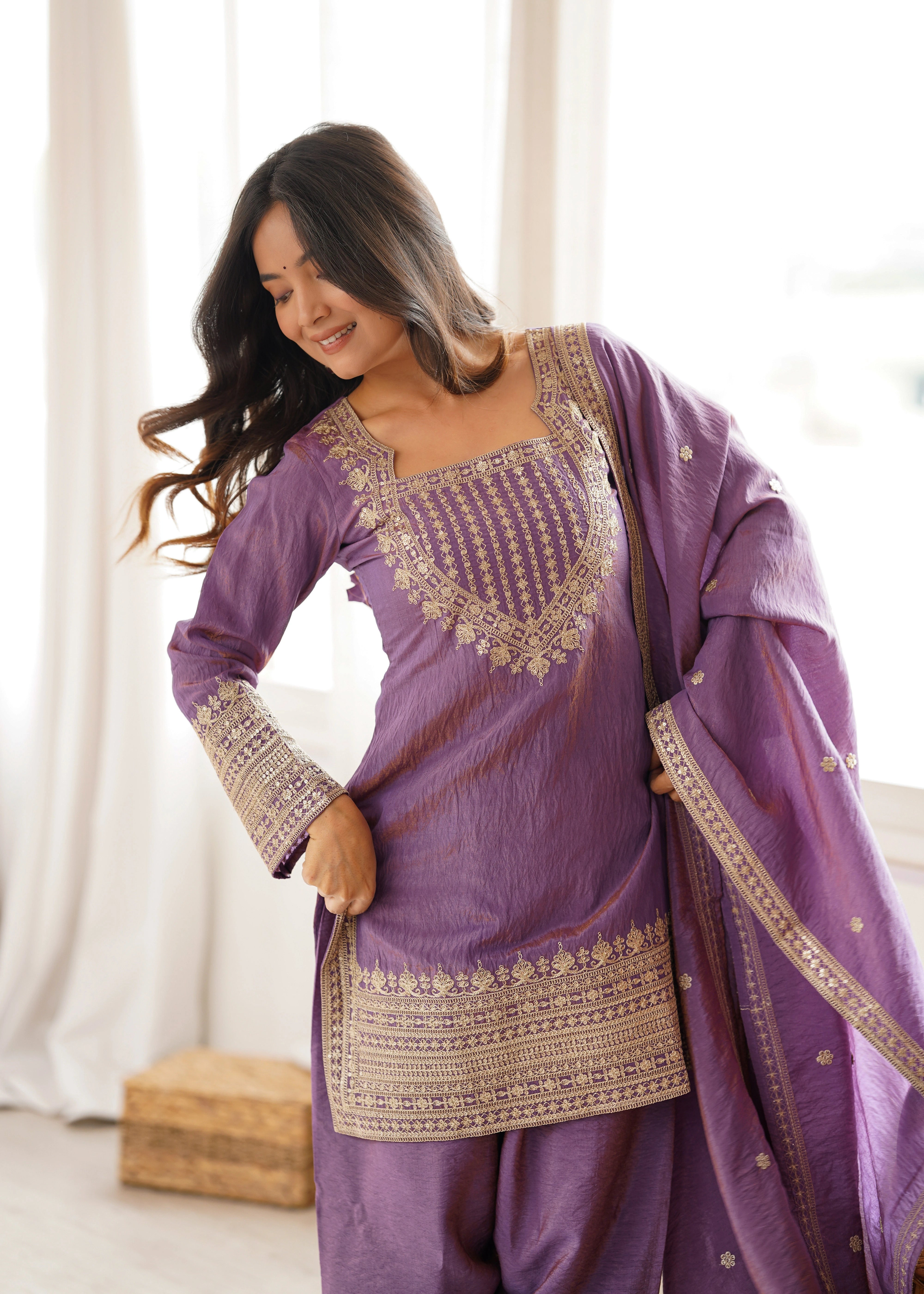 Woman wearing a purple traditional outfit with gold embroidery indoors.