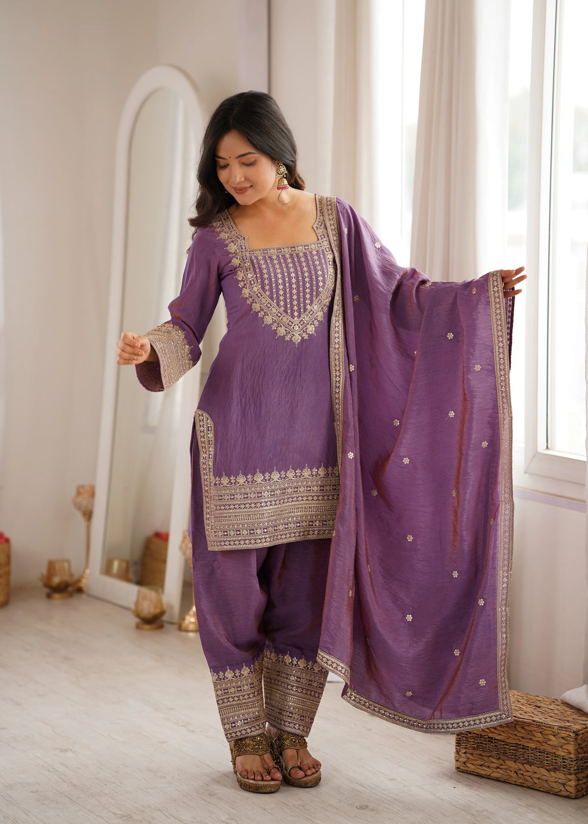 Woman in a purple traditional outfit with gold embroidery standing in a well-lit room.