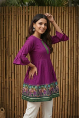 Woman wearing a purple dress with green accents against a wooden fence background