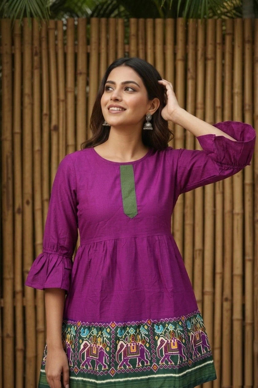 Woman wearing a purple dress with green accents against a wooden fence background