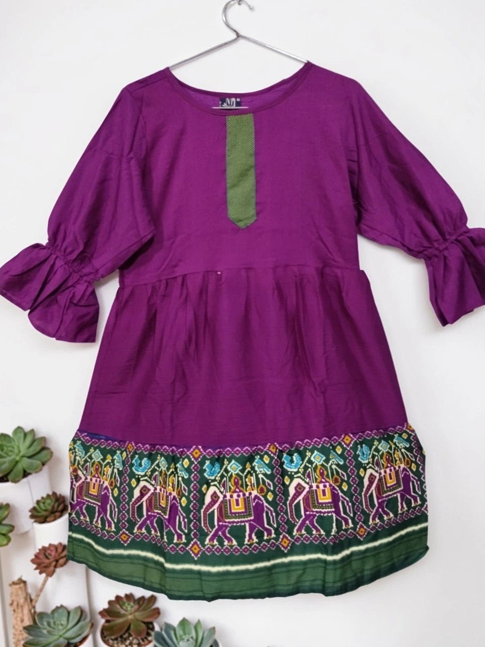 Purple dress with green accents and elephant embroidery on a white background