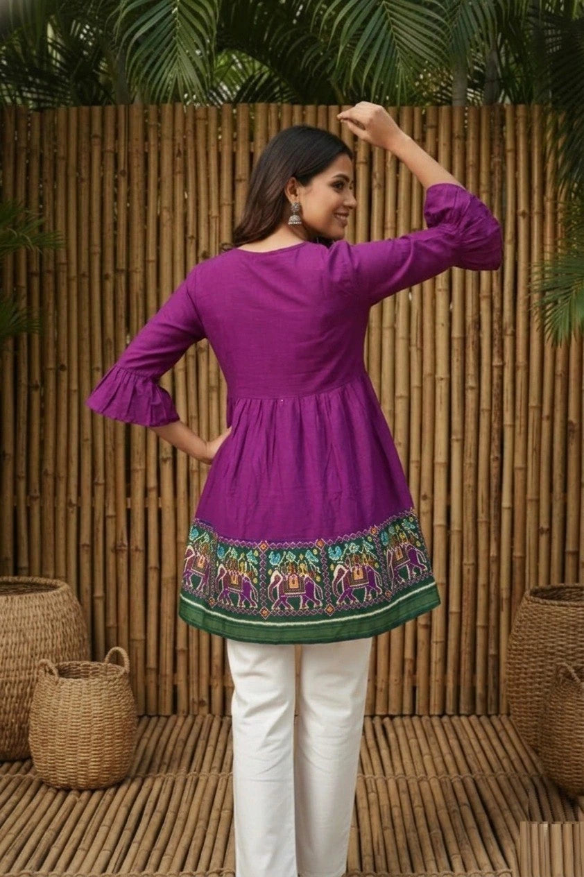 Woman wearing a purple top with colorful hem design against a wooden panel background