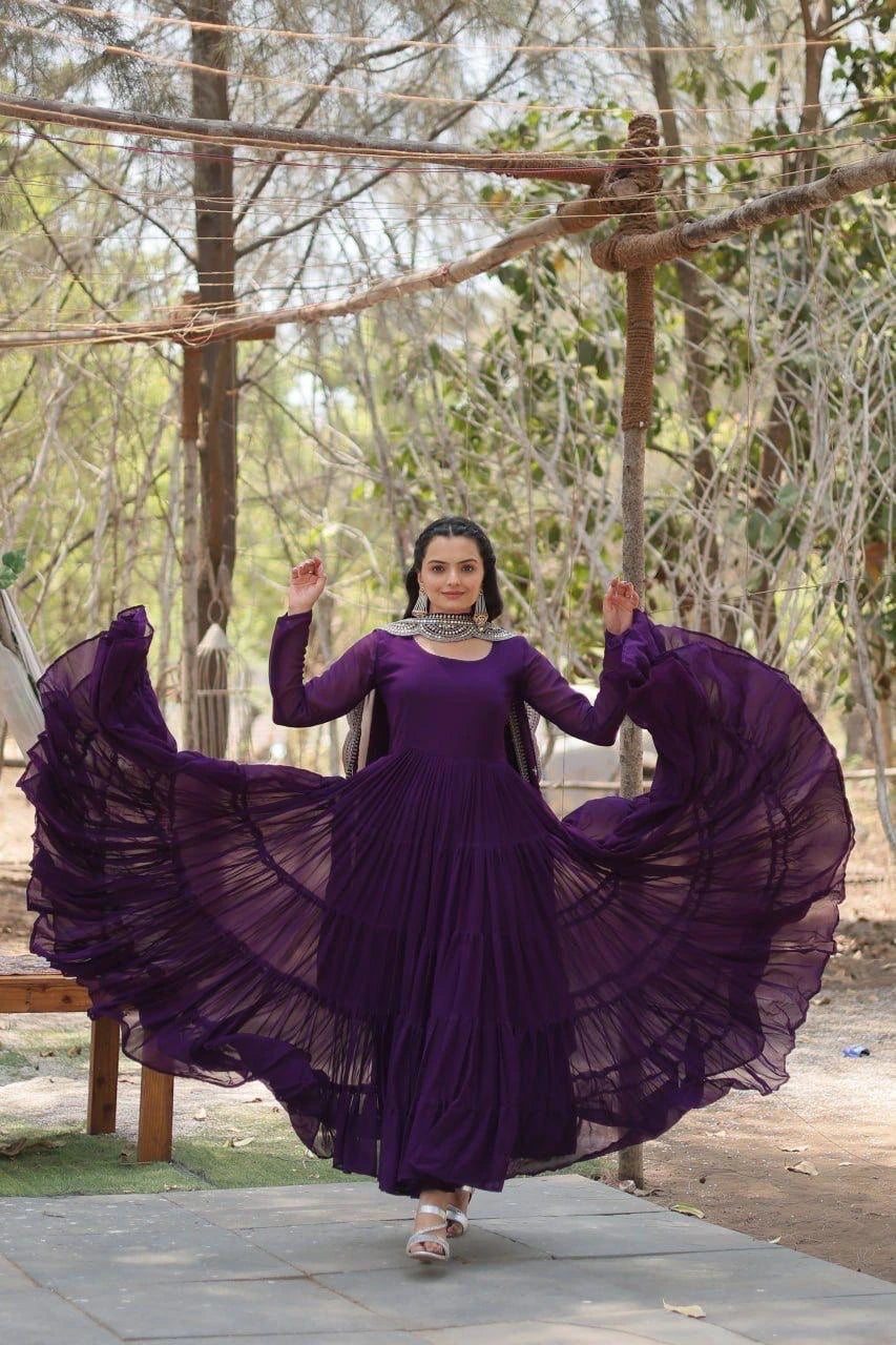 Woman in a long, flowing purple dress standing outdoors with trees in the background