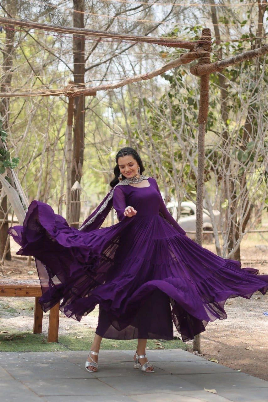 Woman in a purple dress twirling outdoors with trees in the background